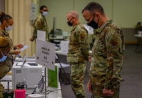 Airmen stand in front of check-in tables.