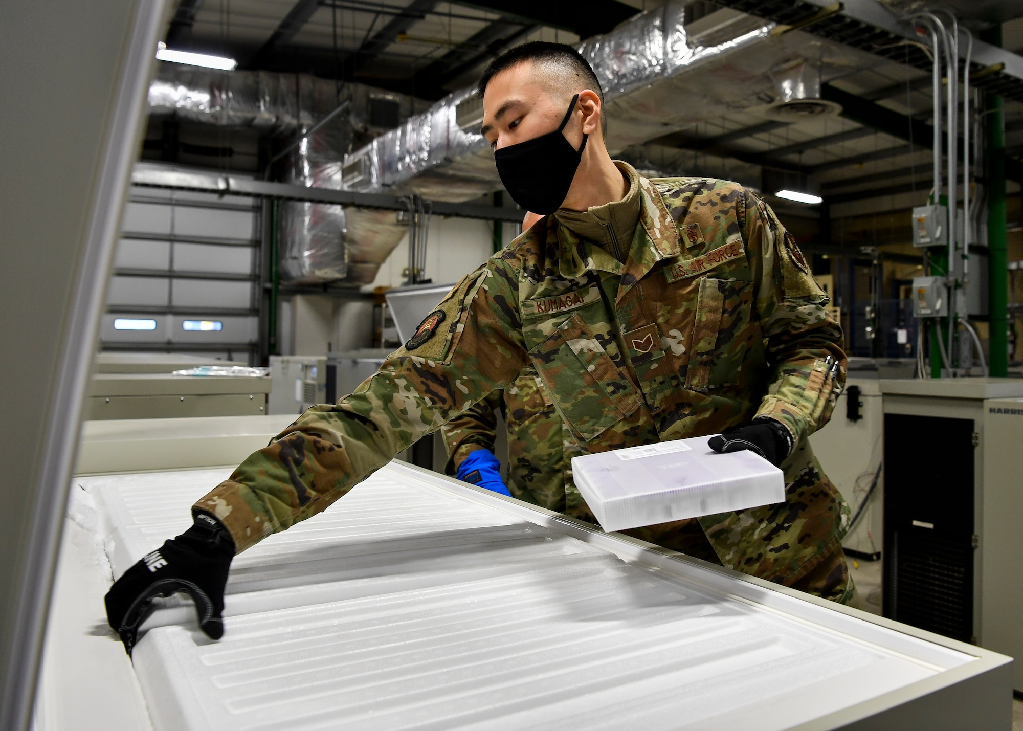 U.S. Air Force Staff Sgt. Akira Kumagai, Armed Services Whole Blood Processing Laboratory – East member, places a batch of COVID-19 vaccines inside a freezer on Joint Base McGuire-Dix-Lakehurst, New Jersey, Dec. 31, 2020. The vaccines, which must be temperature controlled, were placed into freezers before being sent to the McGuire Fitness Center for distribution. (U.S. Air Force photo by Staff Sgt. Jake Carter)