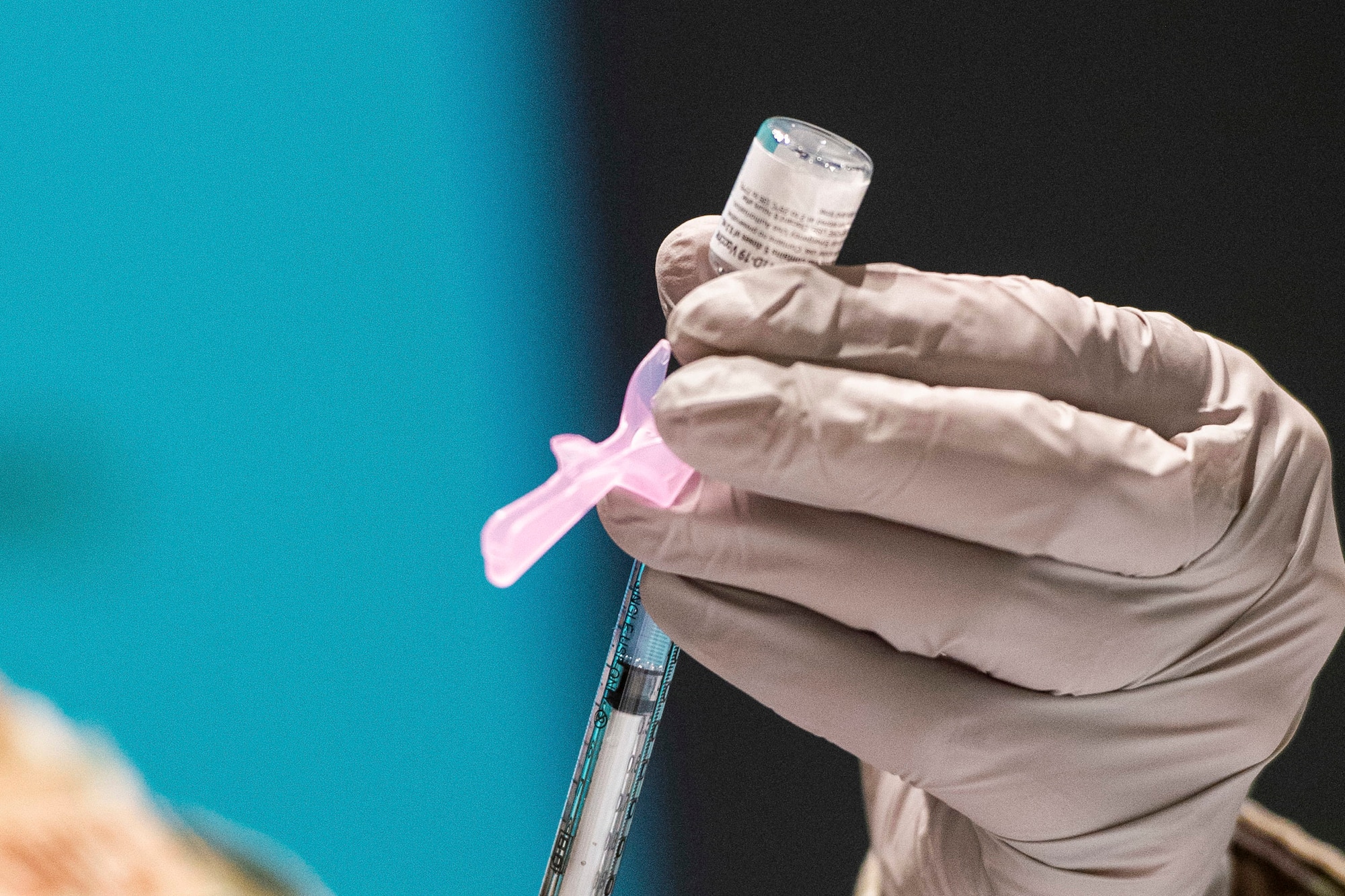 A gloved hand holds a syringe and a small bottle of vaccine.