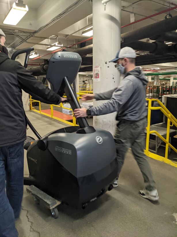 Two men move fitness equipment up a ramp