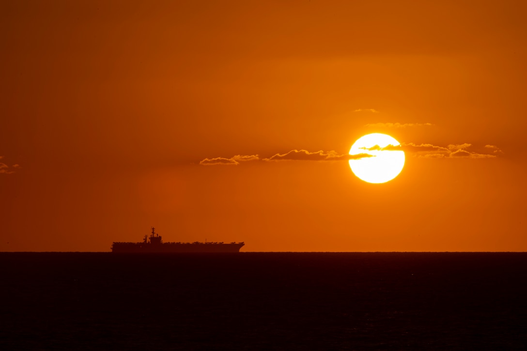 A ship sails on the ocean amid an orange horizon.