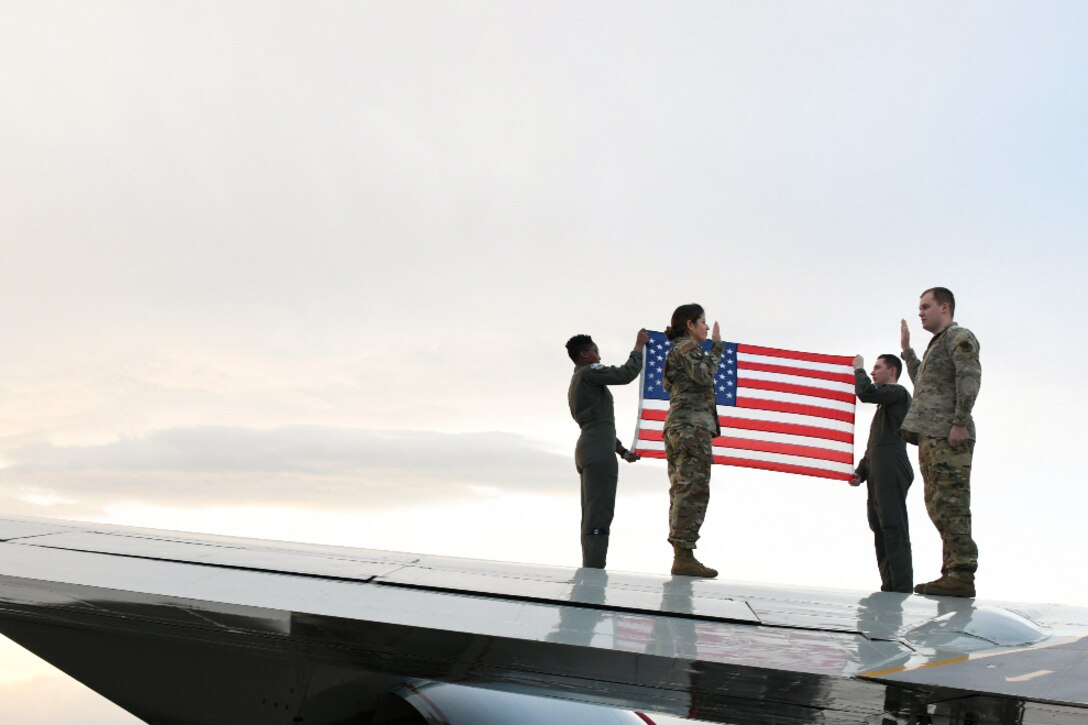 Two sailors participate in a re-enlistment ceremony on an aircraft’s wing as other two service members hold an American flag in the background.