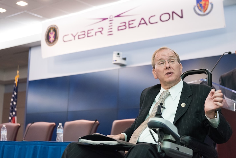 A man in a motorized wheelchair addresses an offscreen audience in a conference room.