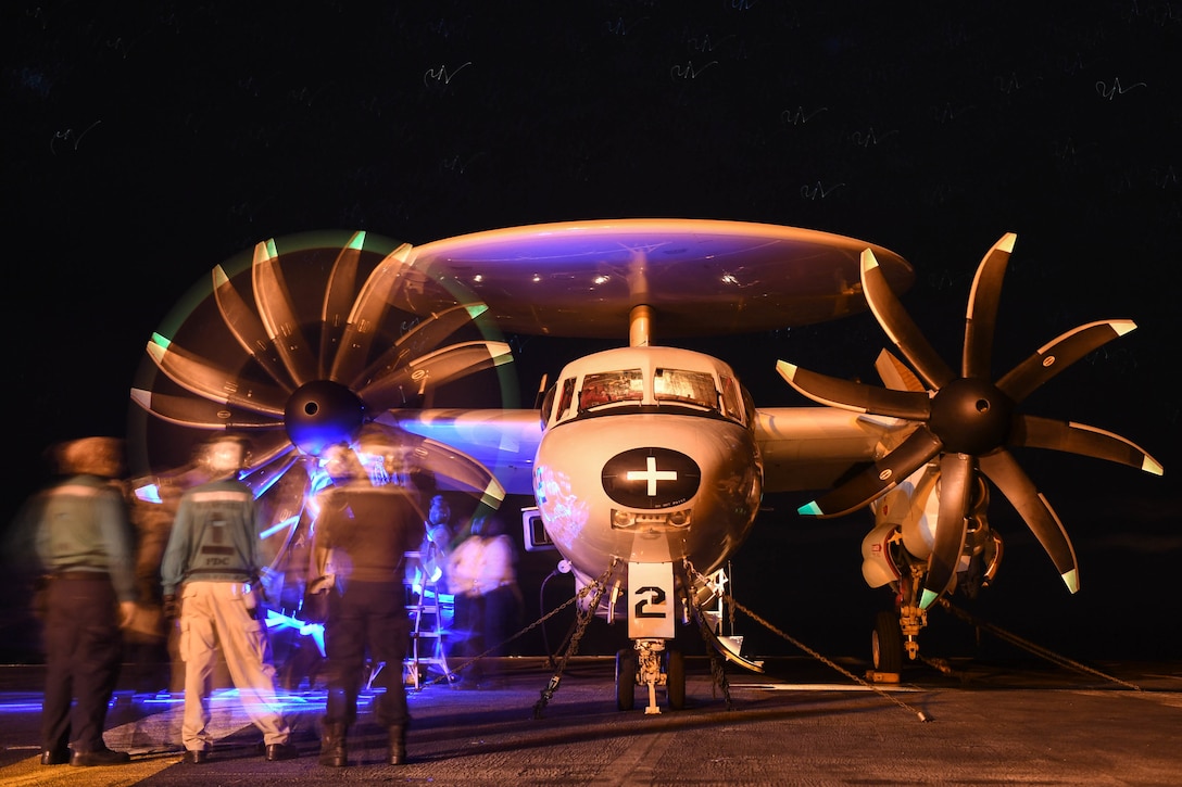 A small group of sailors stand in front of a plane at night.