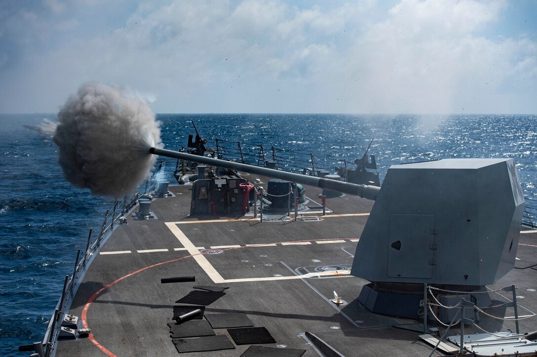 A machine gun creates a smoky cloud as it fires from a ship.