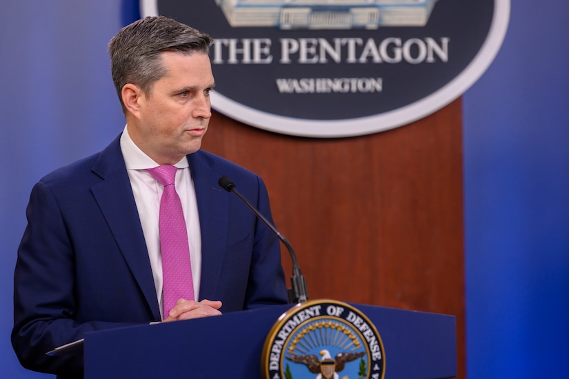 A civilian official speaks at a lectern.