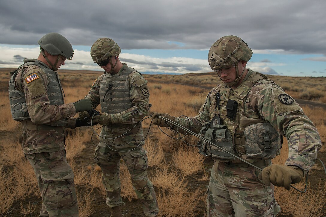 Three soldiers hold wires to prepare for a detonation during training.