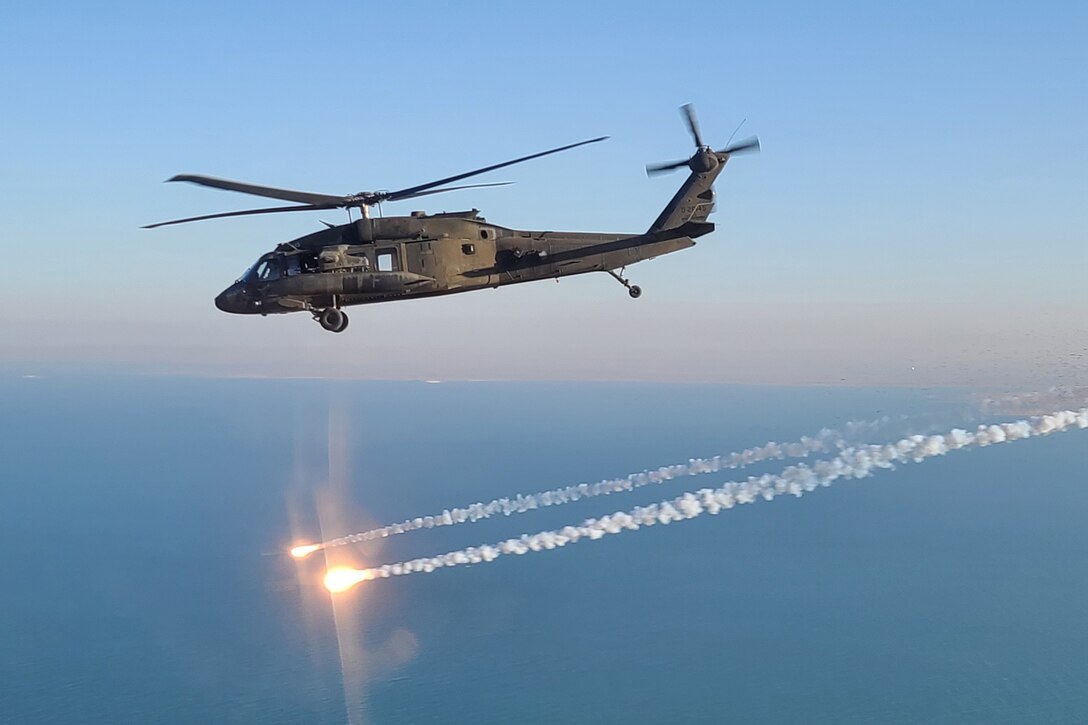 A helicopter flies above flares in the sky.