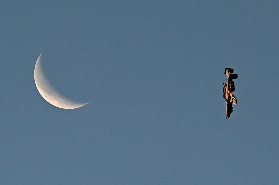 Photo of an A-10 Thunderbolt II flying in the sky with a crescent moon in the background