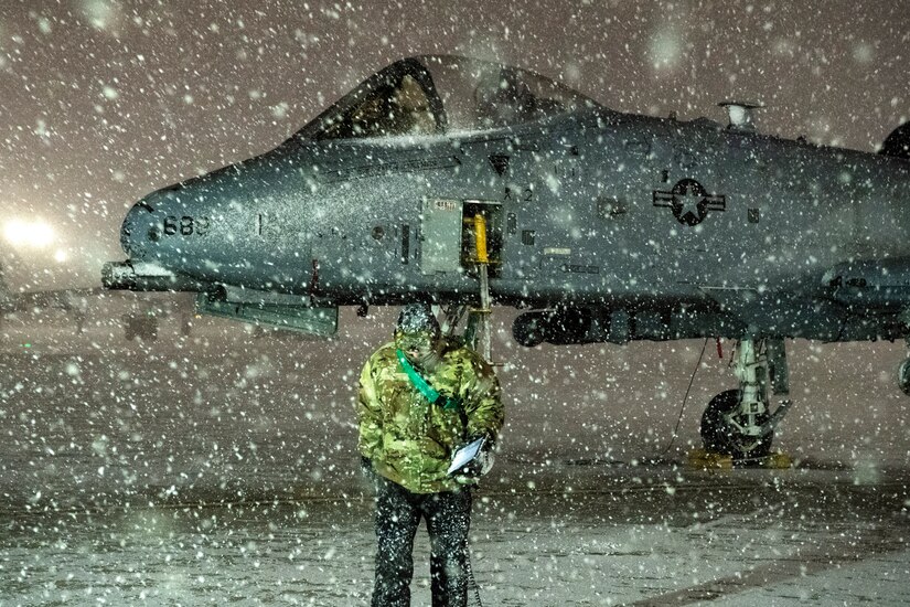 An airman finishes servicing an A-10 while in the snow.