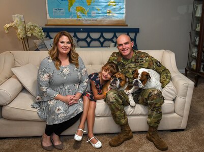 A man, woman and child sitting on a couch with two dogs