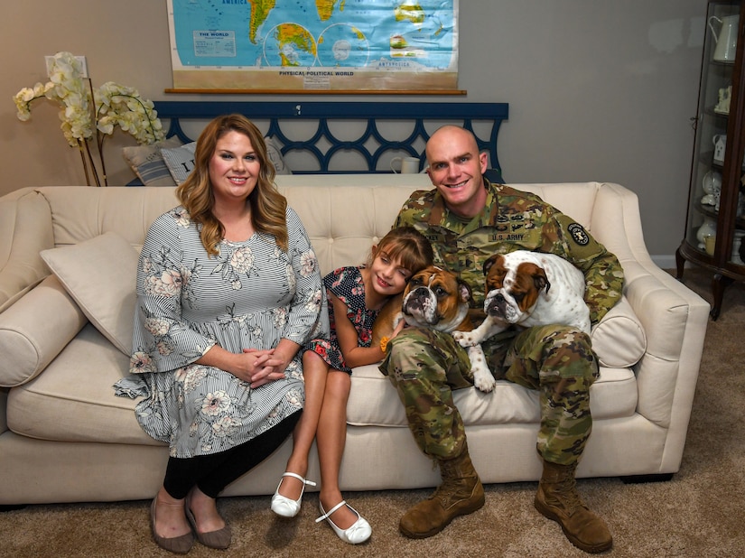 A man, woman and child sitting on a couch with two dogs