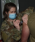 Senior Airman Sara Basiliere injects Spc. Bareden Langmaid with a dose of COVID-19 vaccine during the Vermont National Guard's vaccine rollout at Camp Johnson, Vermont, Jan. 7, 2021. Langmaid, a construction equipment repair specialist with Echo Company, 5-72nd Brigade Engineer Battalion, said he received the shot to help mitigate his COVID-19 risk while he works on sample testing. Basiliere is an immunology specialist with the Vermont Air National Guard's 158th Medical Group.