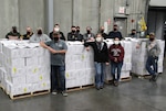 14 employees wearing face masks stand around pallets of shipping boxes.