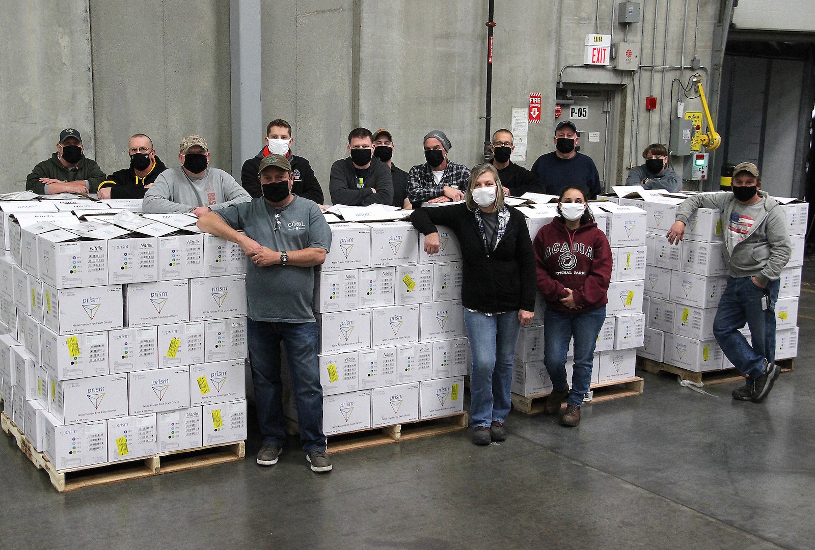 14 employees wearing face masks stand around pallets of shipping boxes.