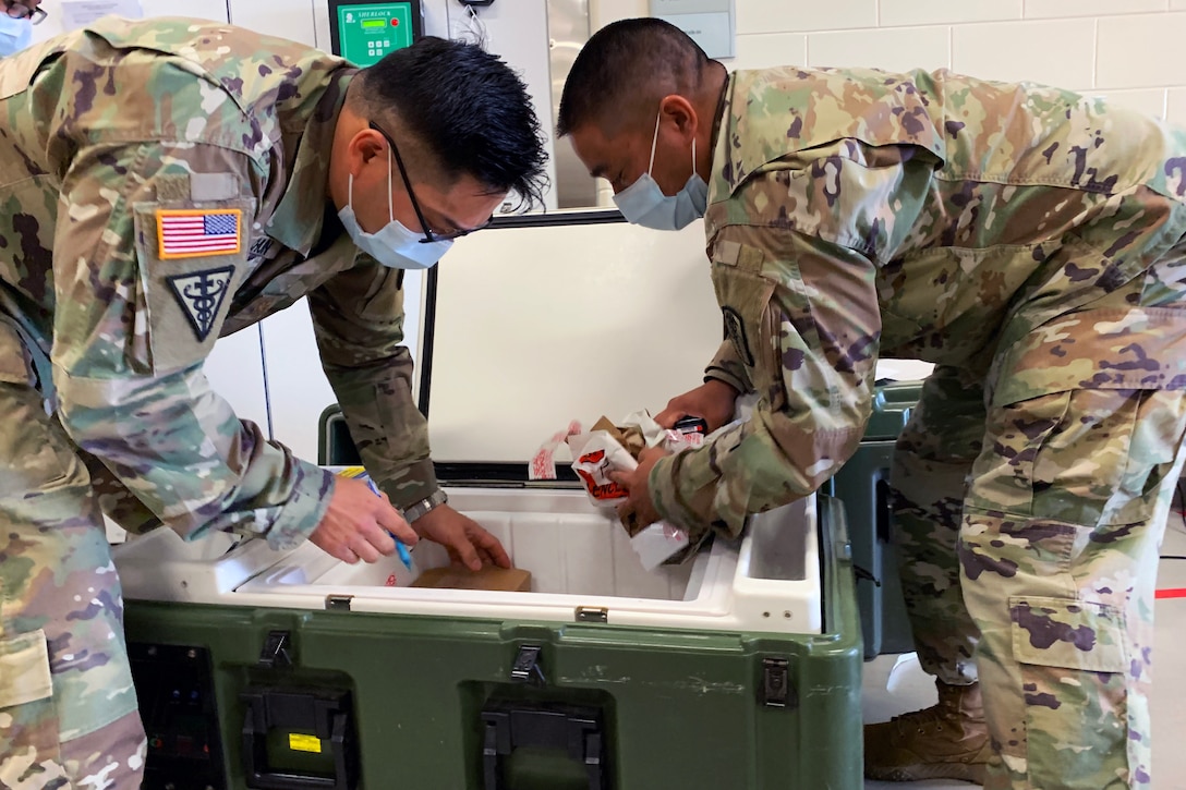 Two army soldiers put COVID-19 vaccines in a cooler.