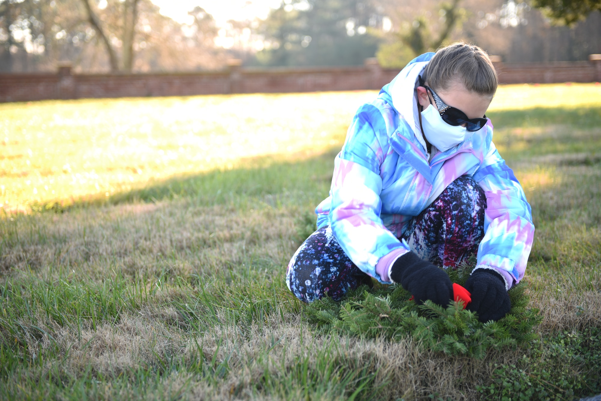 Military child straightens the bow on a wreath covering a headstone.