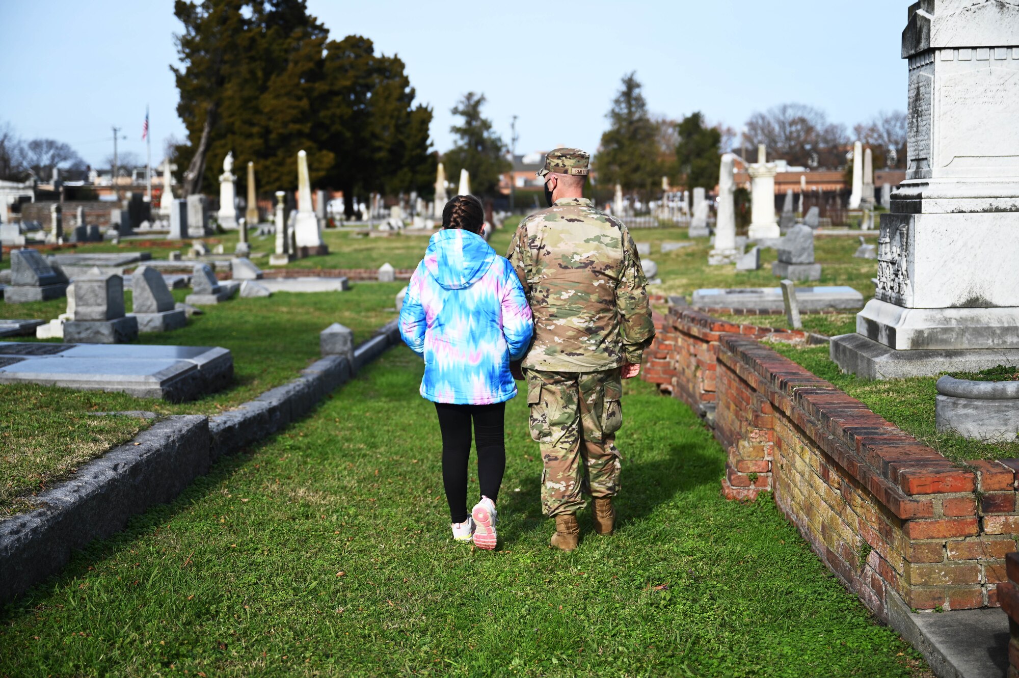 Airman walks with his daughter through cemetery to honor fallen veterans.