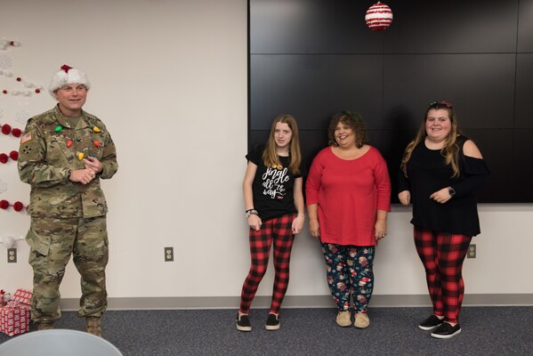Robyn Ratchford, 20-year volunteer at the Middle East District, stands between her two daughters and major helpers following a successful 2019 holiday party for the District, while TAM Commander COL Philip Secrist in holiday garb, applauds their efforts, ingenuity, and creativity. Ratchford is the backbone and heavy muscle of the District's Employees Activities Association.