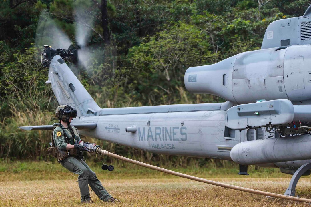 A Marine pulls a hose along the grass next to a parked helicopter.