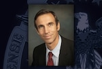 Head and shoulders image of a white man wearing red tie, white shirt and black suit jacket.