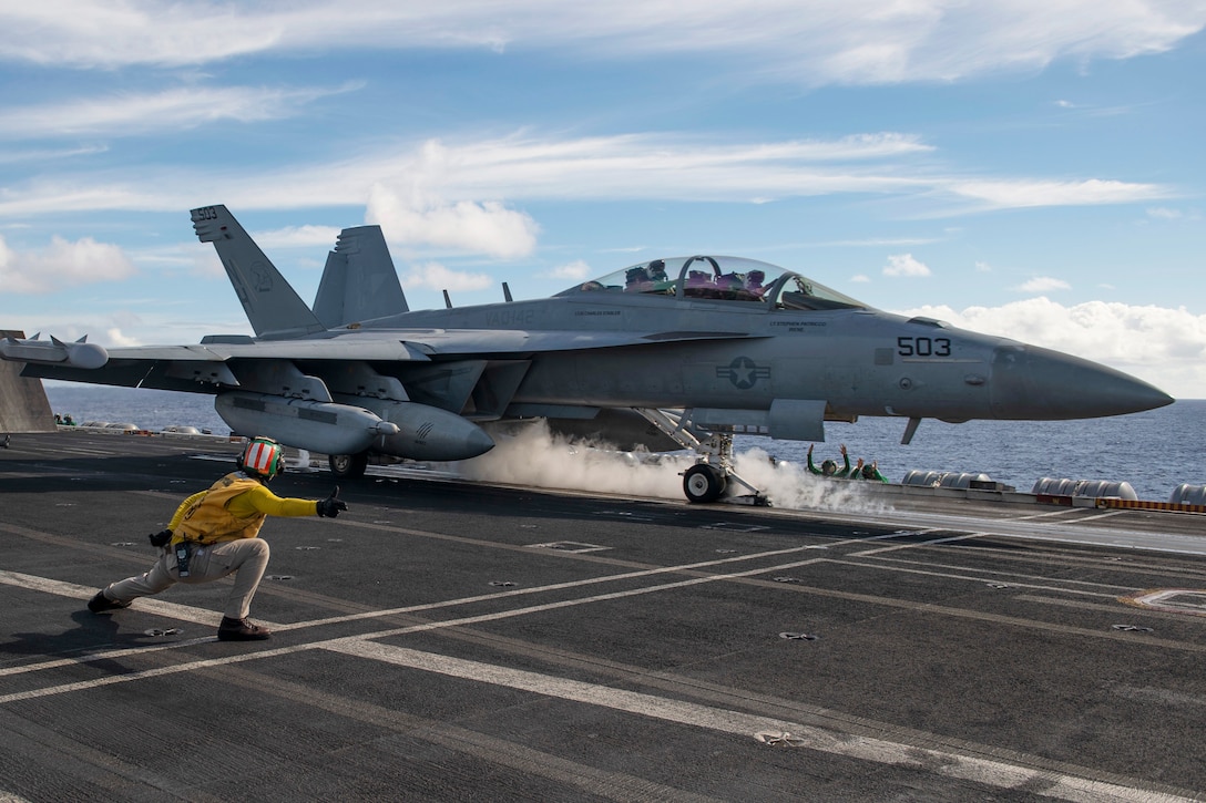A sailor signals a fighter jet to take off from the deck of an aircraft carrier.