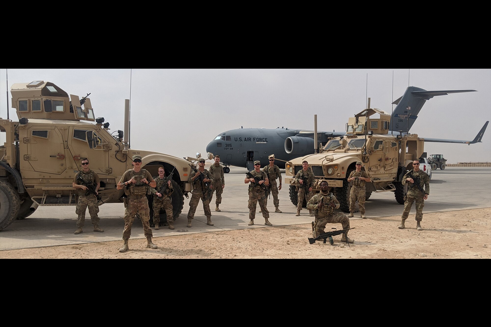 Photo shows military members standing in front of two humvees and a C-17 aircraft in the desert.