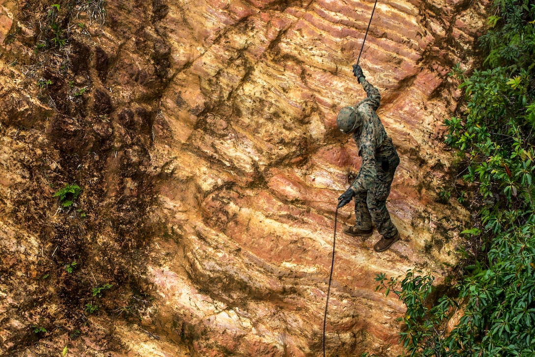 A Marine rappels down a  ridged rocked formation.