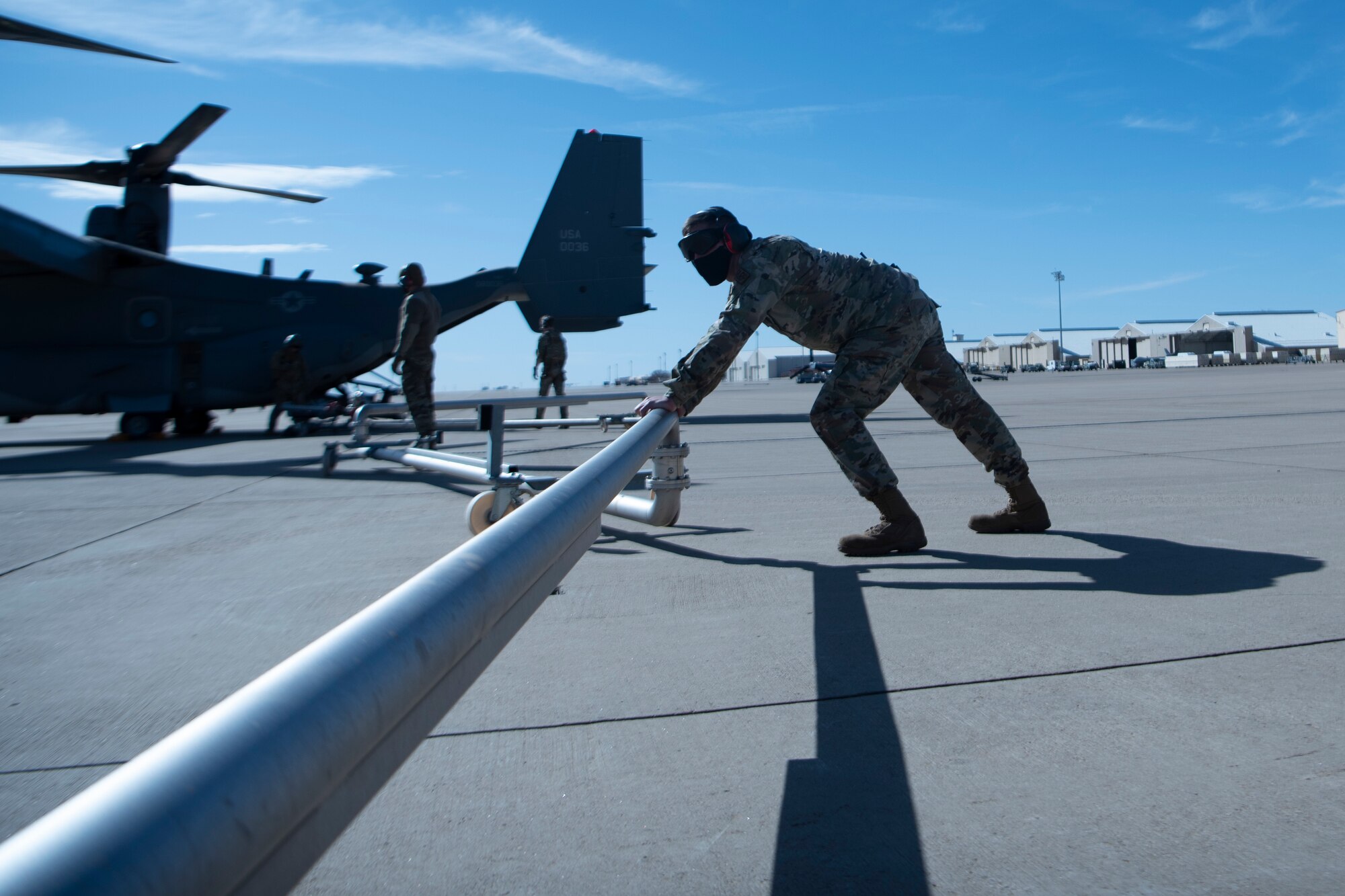 An Airman pushes a metal pipe in place to fuel a plane