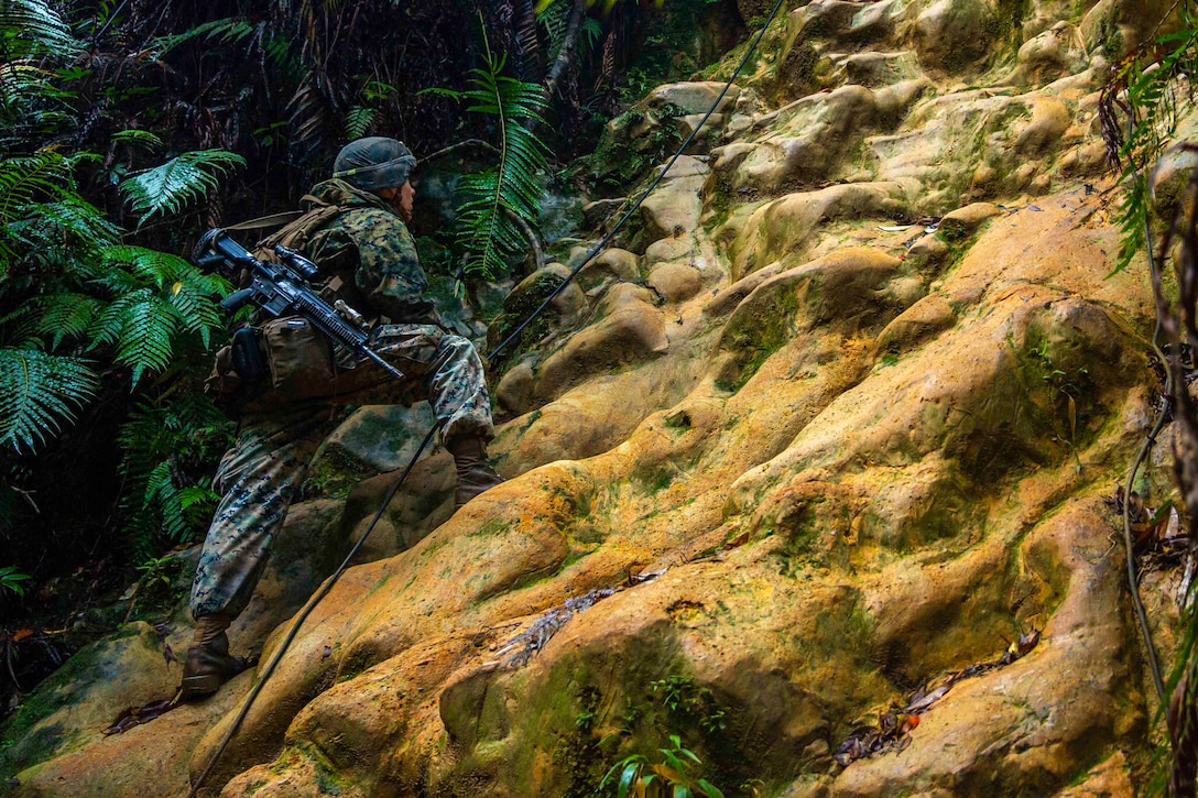 A Marine moves up steep terrain while holding a rope.