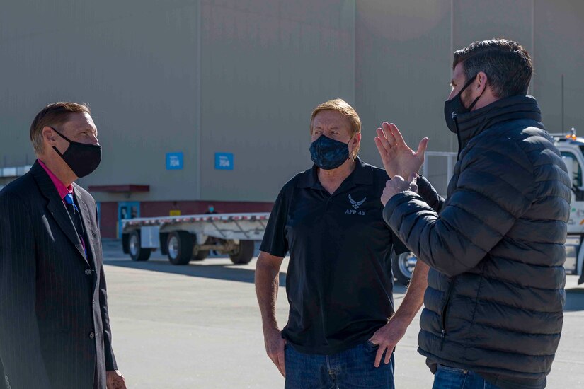 Three men in face masks have a conversation.