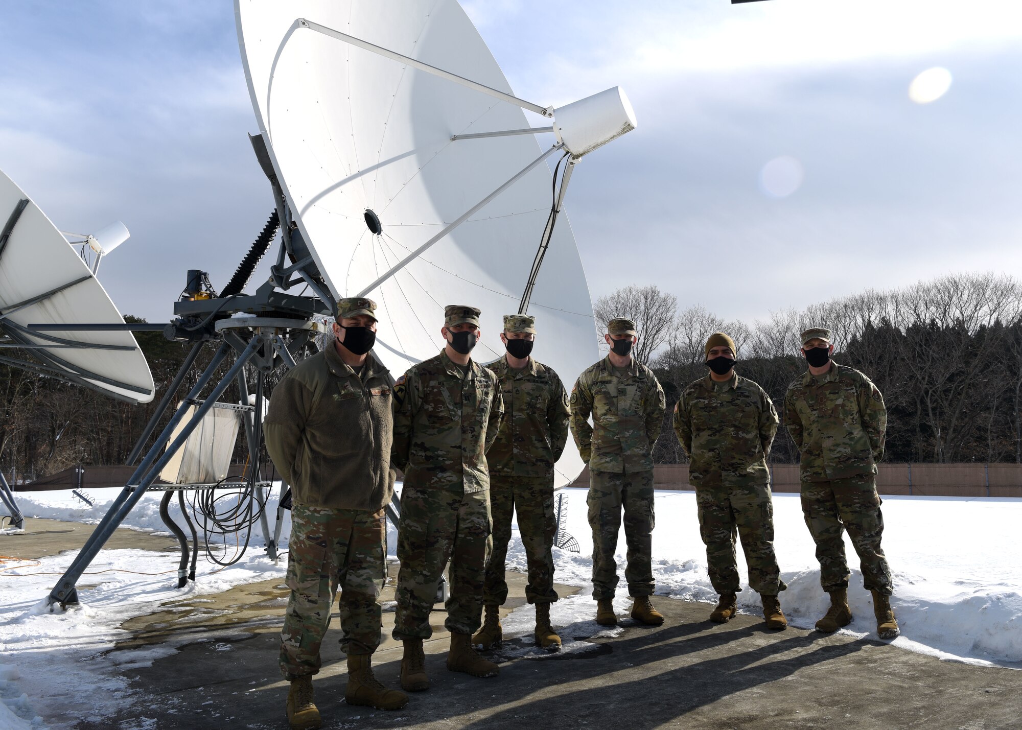Individuals stand in front of a radar for a group photo outside during winter