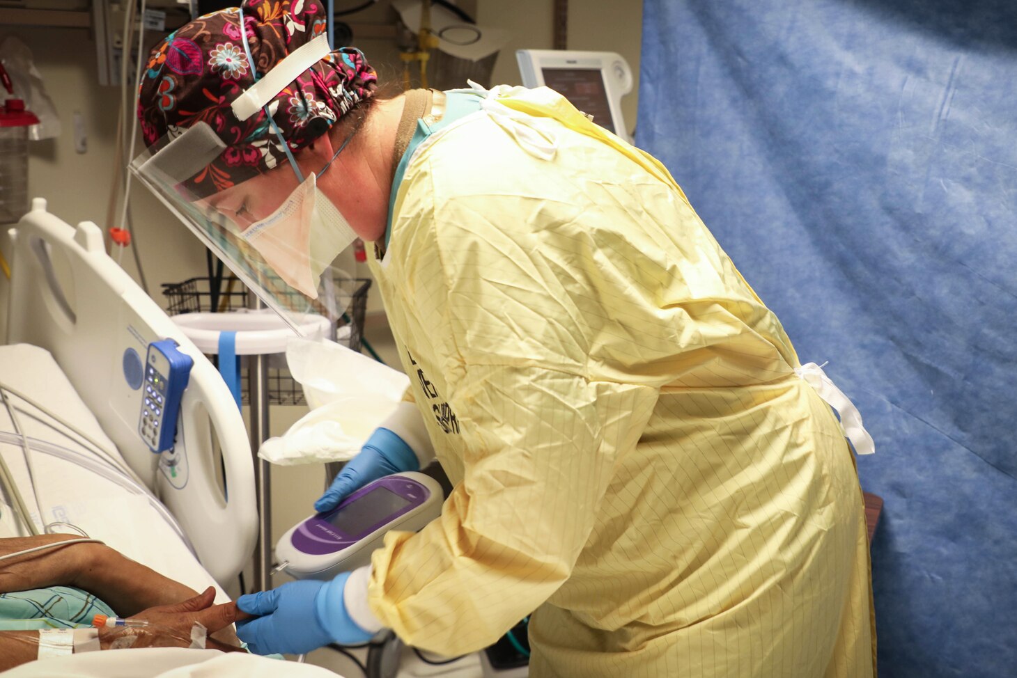 A nurse wearing personal protective equipment checks a patient.
