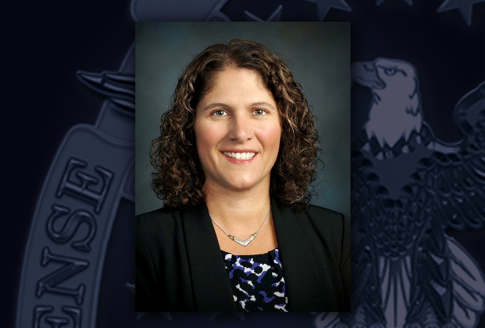 Head and shoulders image of a white woman with dark hair in a blue/white printed top and a black suit jacket.