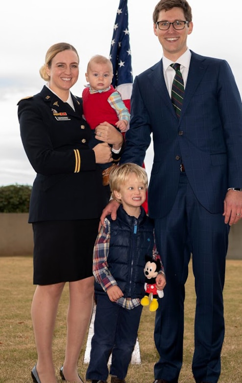 A woman holding an infant stands with a man and child