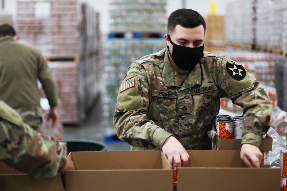 A soldier wearing a face mask packs food boxes at an emergency food network warehouse.