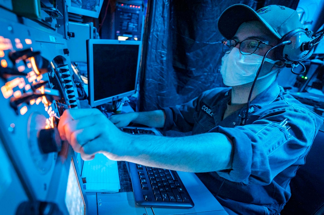 A sailor sits in a darkened room in front of an array of instruments.