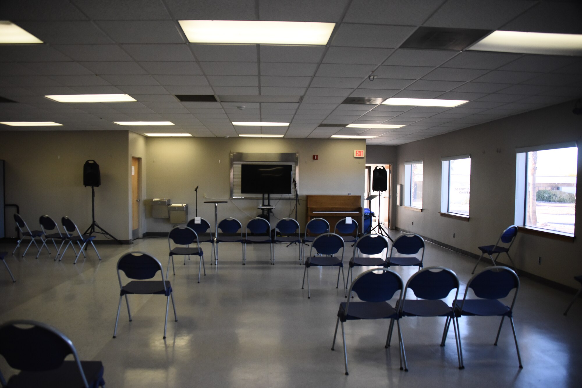 A large room with folded chairs, a piano, and a tv screen.
