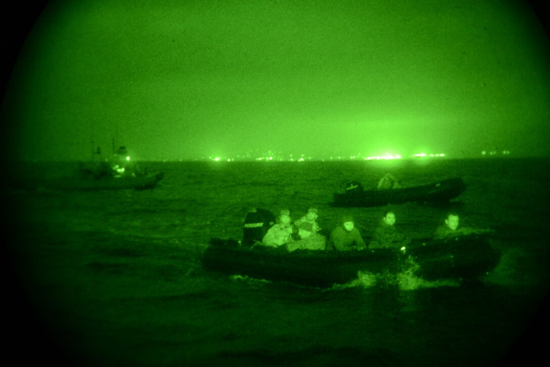 Service members move through the water in inflatable boats.