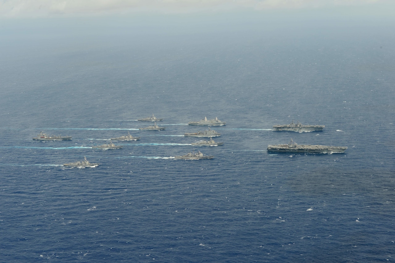 A dozen Navy vessels move through the ocean.