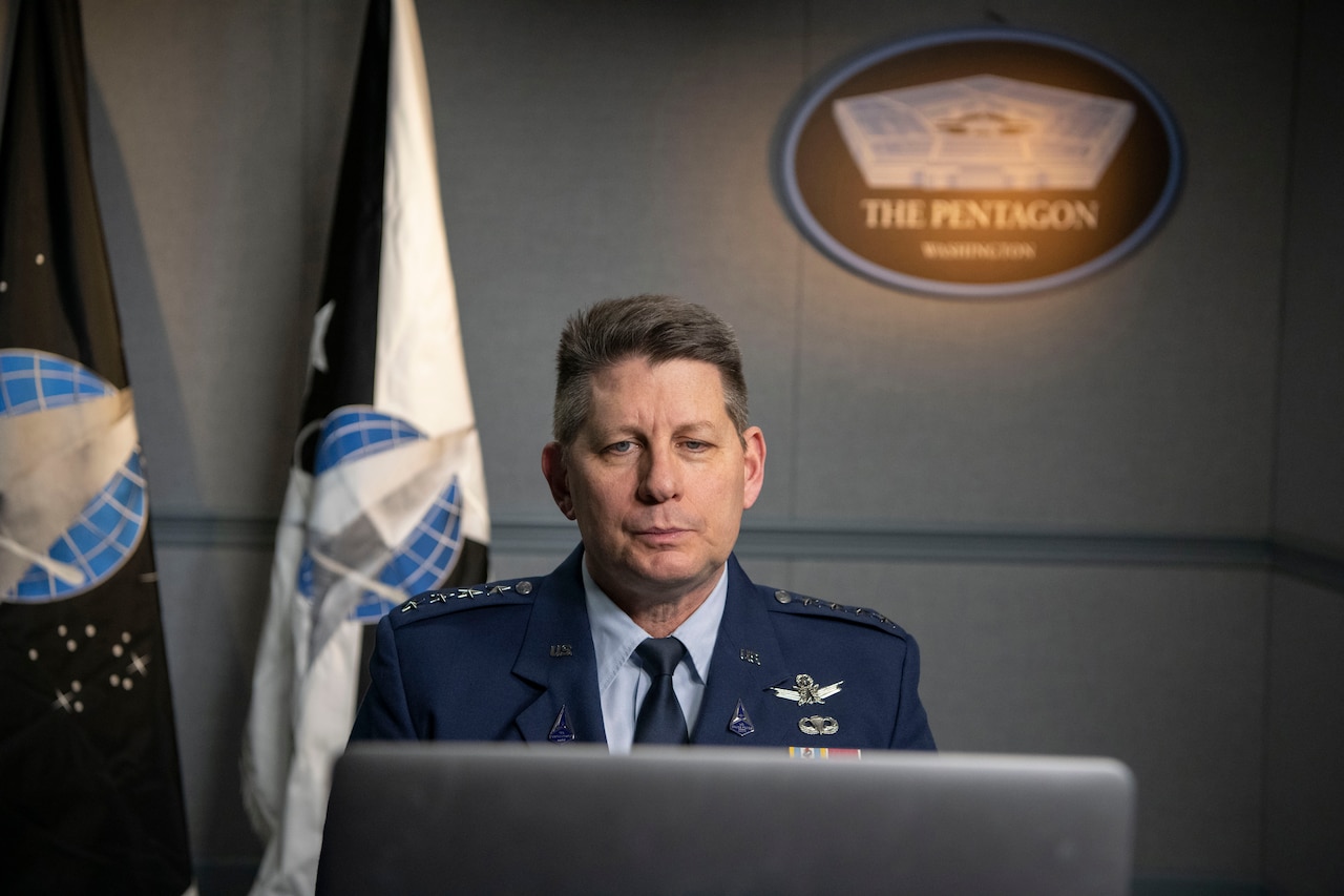 A man in a military uniform, sitting at a computer, is speaking during a virtual meeting.