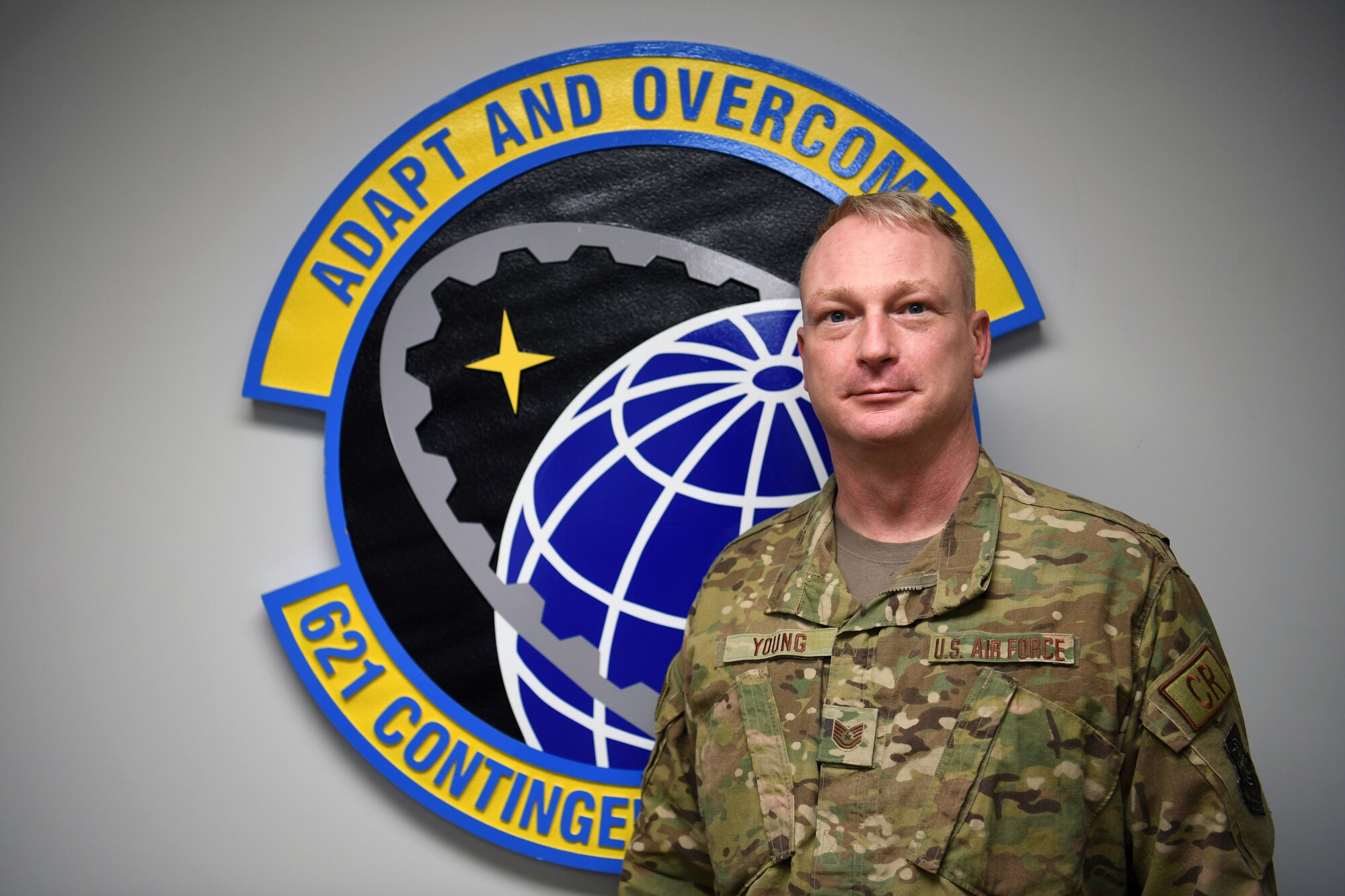 Tech. Sgt. Kelly Young, 621st Contingency Response Squadron self-inspection program manager, poses in front of his squadron emblem at Joint Base McGuire-Dix-Lakehurst, New Jersey, Jan. 13, 2021. Young is active around the base and in his squadron with various programs that help Airmen and their families. (U.S. Air Force photo by Tech. Sgt. Luther Mitchell Jr.)