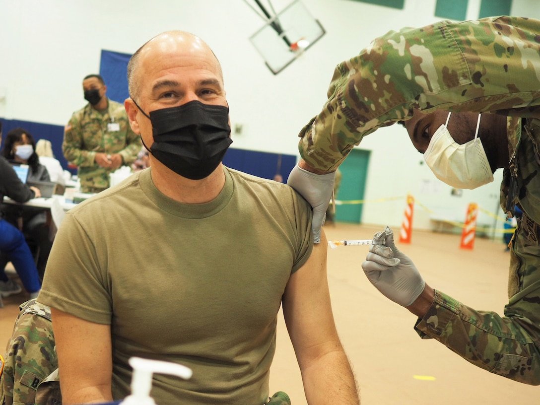 A man in a mask receives a shot from a soldier.