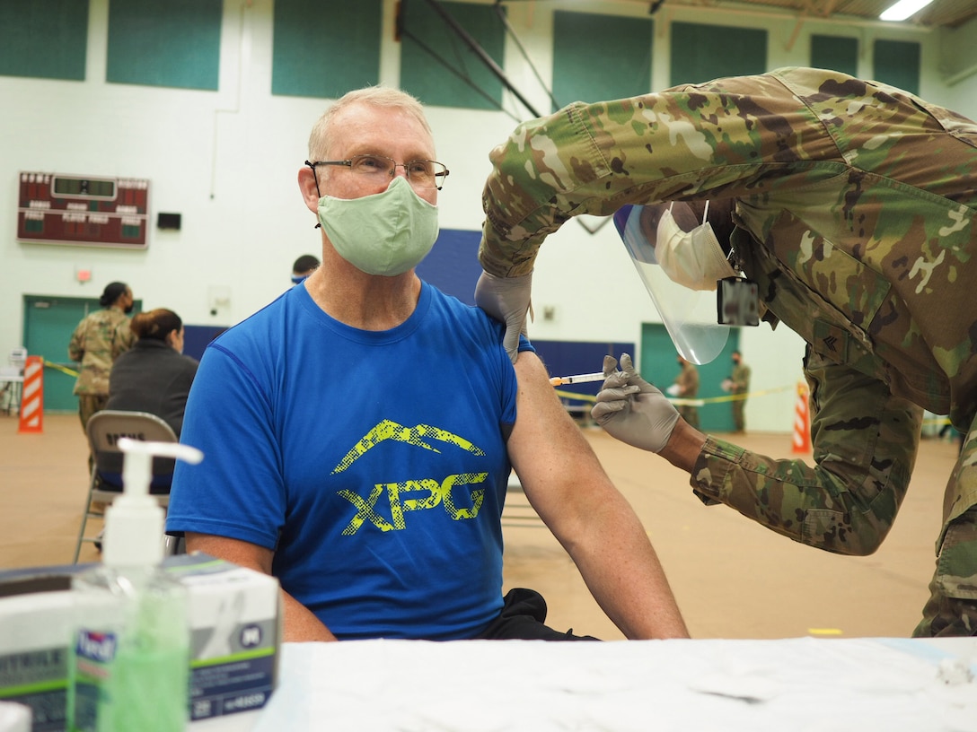 A man in a mask receives a shot from a soldier.