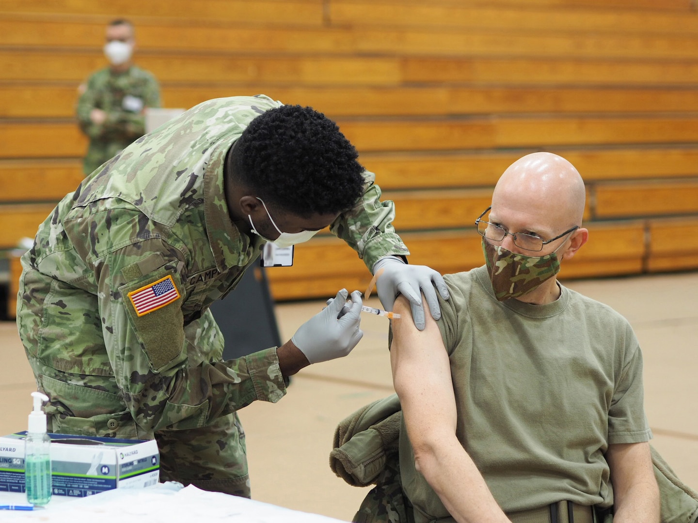 A man in a mask receives a shot from a soldier.