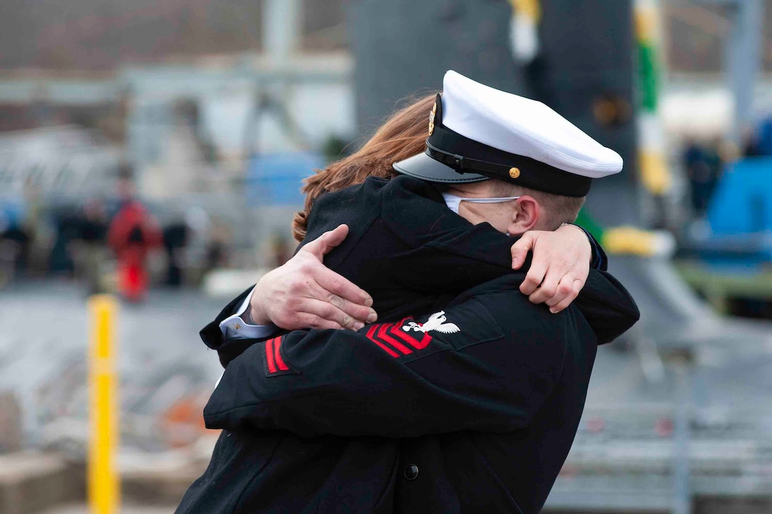 A sailor hugs a woman in a tight embrace.