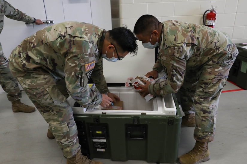 Two male servicemembers remove medical supplies from a cooler.