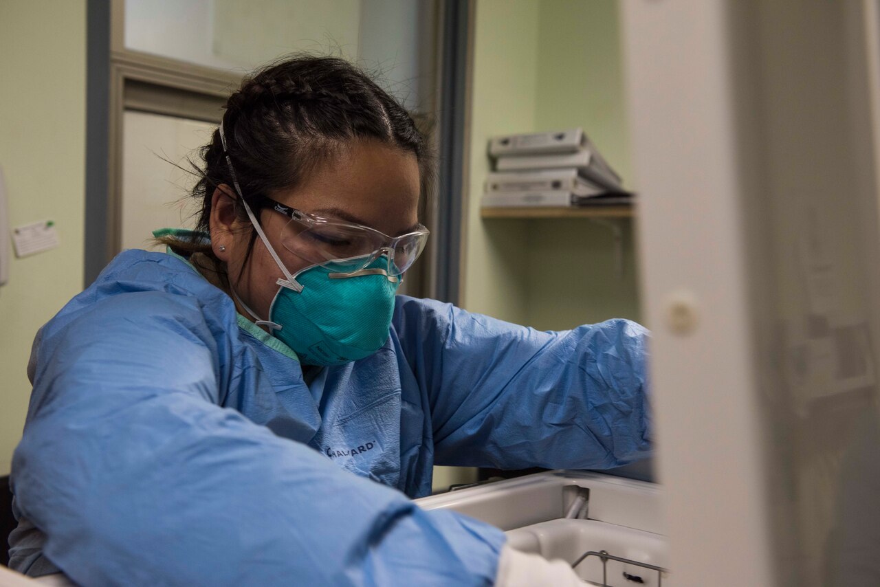 A woman wearing personal protective equipment opens a cooler.