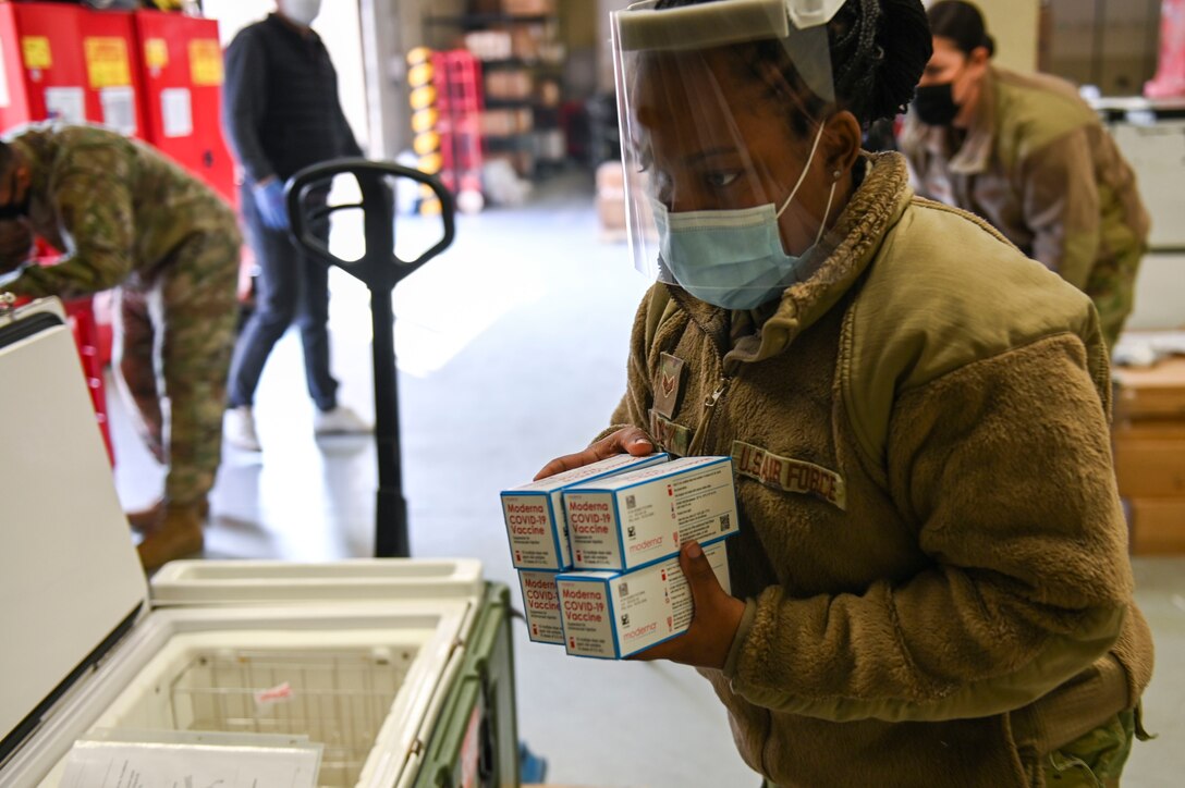 A female servicemember removes vaccines from a cooler.