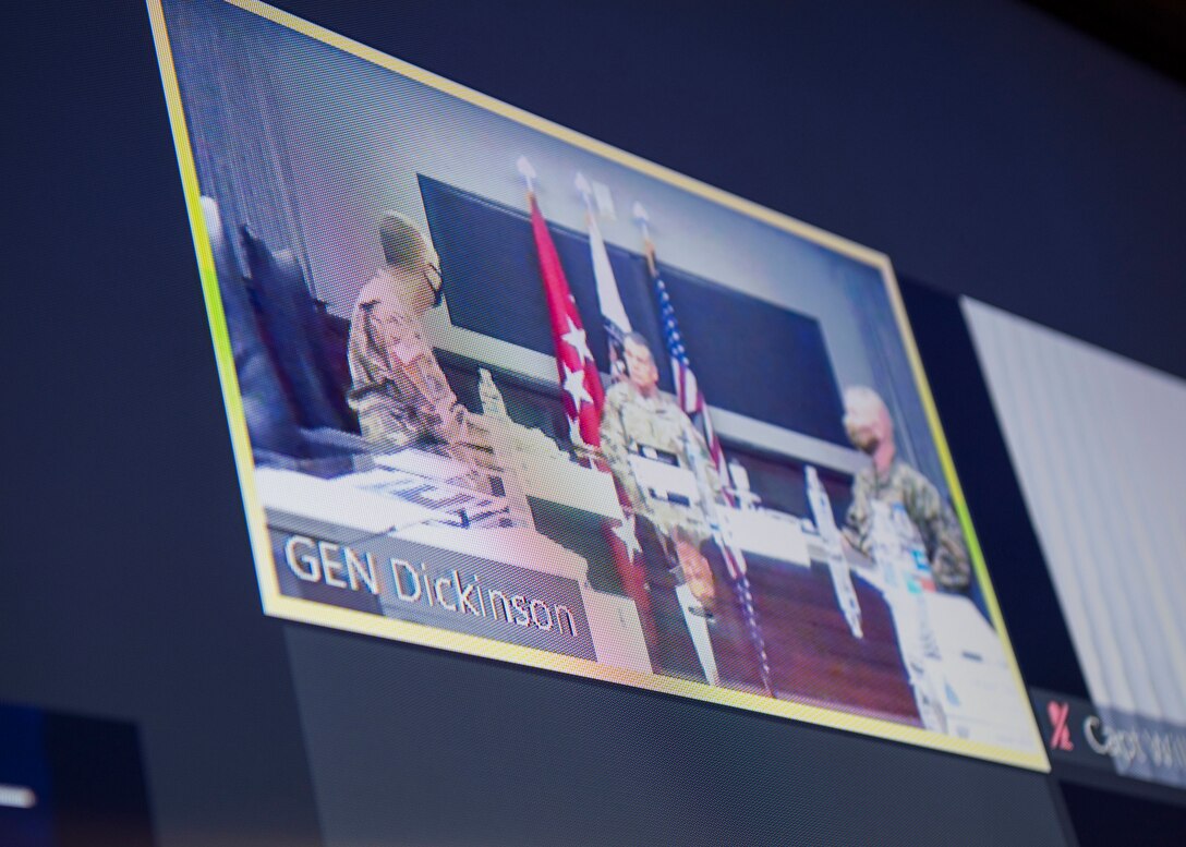Picture of t.v. screen with video teleconference shot showing three military personnel sitting at a conference table.